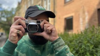 A man in a green sweater takes pictures with the Fujifilm X100VI