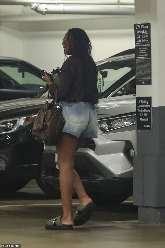 She accessorized with green loafers, a large brown handbag, square glasses, chunky rings and a necklace with a striking round pendant