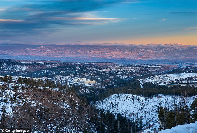 Above is a rural winter photo overlooking Los Alamos, New Mexico at left and center, the Omega Bridge at center, and the Los Alamos National Laboratories at right