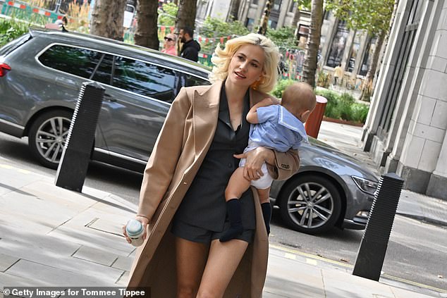 Pixie wore a pair of charcoal grey shorts and a matching plunging blazer under a long camel coat with statement lapels