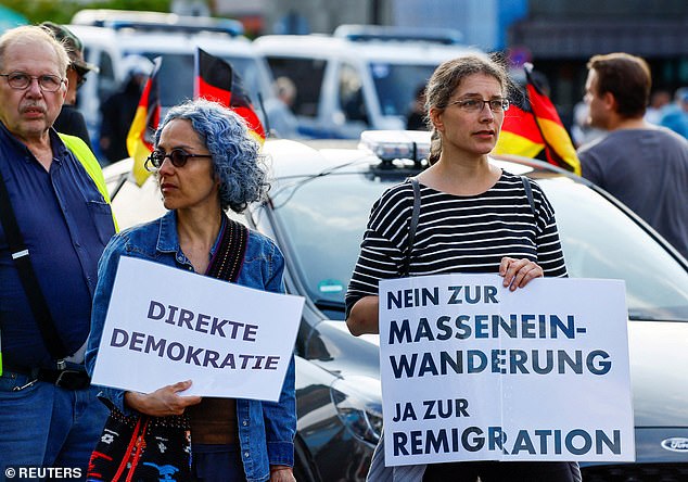 People hold up banners reading 'Direct democracy' and 'No to mass immigration, yes to remigration' as far-right protesters march through the streets of Solingen