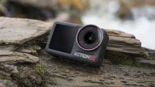 DJI Osmo Action 5 Pro camera on a tree trunk with moving water background