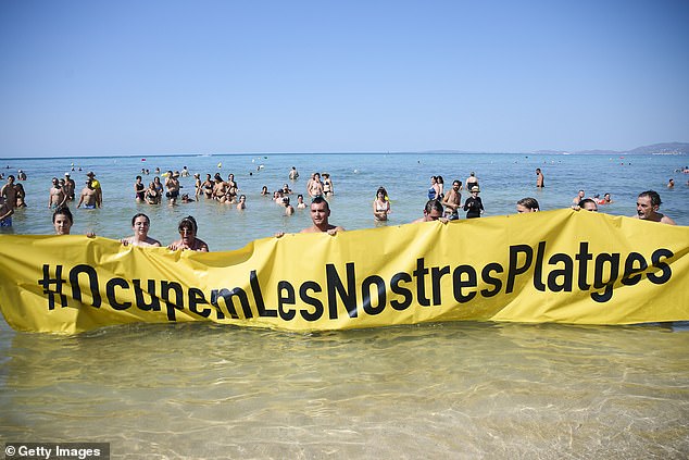 Members of the Mallorca Platja Tour association demonstrate against tourism with a banner reading 'Let's occupy our beaches!' on the beach of Palma de Mallorca on August 11