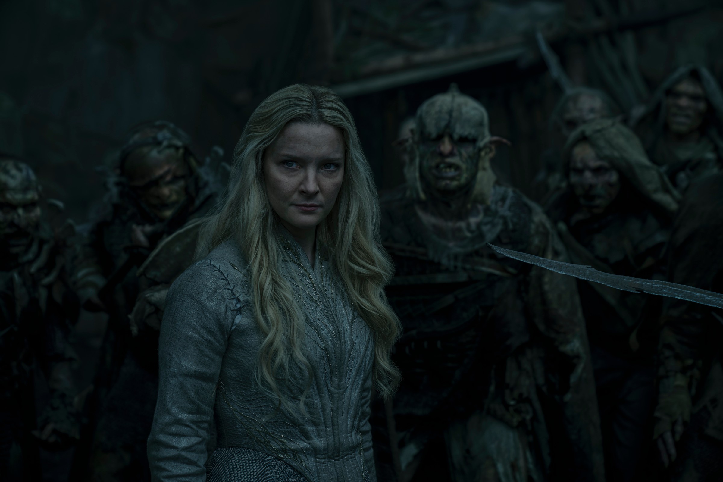 Morfydd Clark as Galadriel in Lord of the Rings: The Rings of Power, standing in full armor before a group of orcs