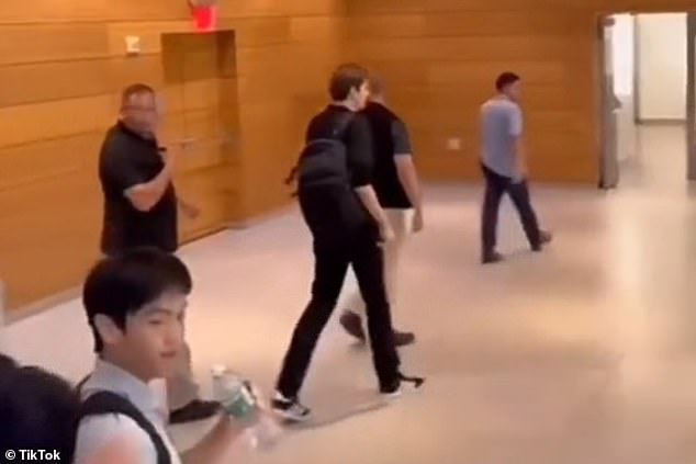 Clearly visible in the video is his cadre of officers guiding him through the halls and classrooms of NYU, a constant presence both a few steps ahead of him and a few steps behind him.