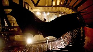 Batman slides down a flight of stairs to avoid gunfire in Batman Begins