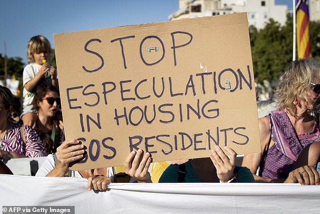 A protester holds up a sign that reads 'stop speculation in housing, SOS residents'