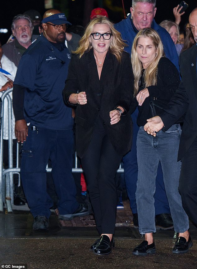 Kate accessorized the oversized jacket with a pair of navy trousers and black loafers. She accessorized with black square-framed glasses and gold earrings.