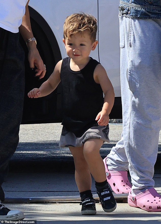 The cute little baby wears a black tank top and black sneakers with velcro closures during the outing with his parents