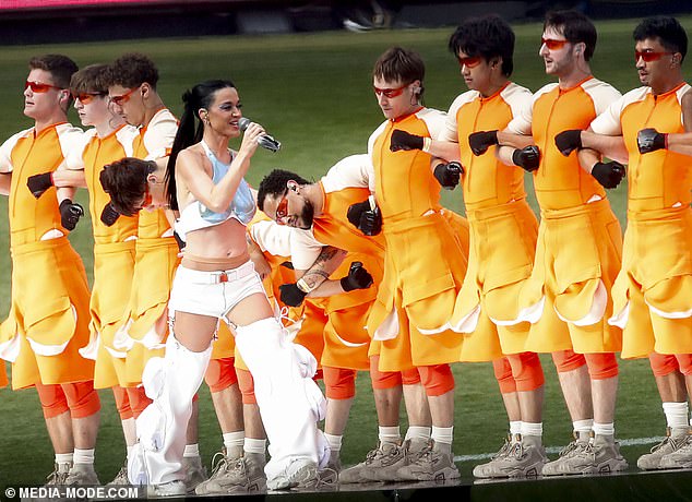 She was surrounded by a line of male dancers dressed in futuristic orange and white outfits