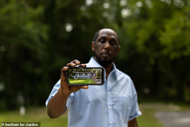 The devastated homeowner holds up a photo of what his property looked like before it was demolished