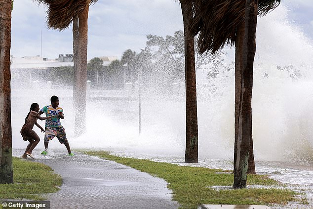 People are splashed by the swirling surf from Tampa Bay as Hurricane Helene passes offshore in St. Petersburg, Florida on September 26, 2024. Storm surges are significantly higher and cause more damage