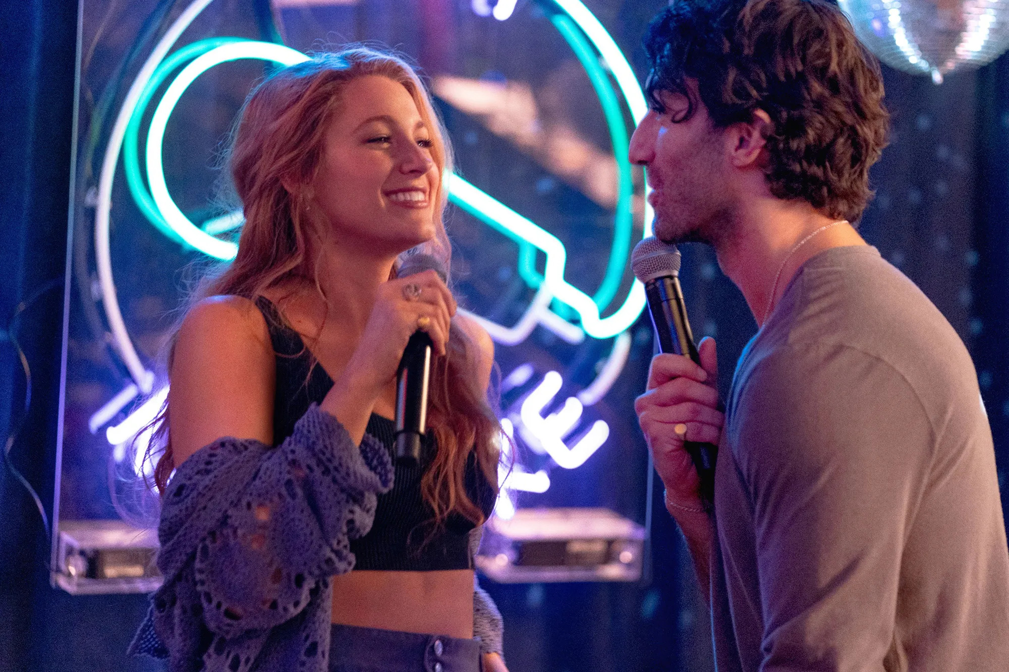 Blake Lively and Justin Baldoni hold microphones in It Ends With Us.