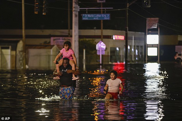 Jamir Lewis wades through floodwaters in the wake of Hurricane Helene with his two daughters, Nylah and Aria, on Friday