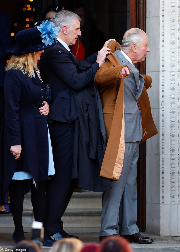 King Charles III's Police Protection Officer helps him put on his greatcoat after a visit to Luton Town Hall, December 2022