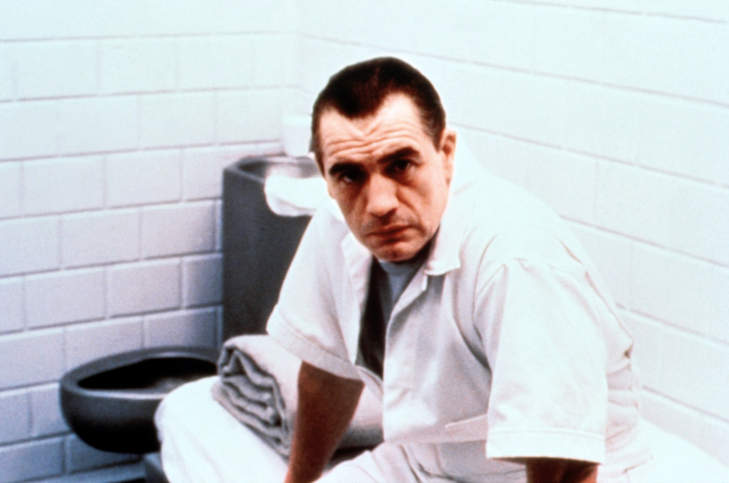 Brian Cox sits in a cell wearing a white prison uniform as Hannibal Lecter in Manhunter 