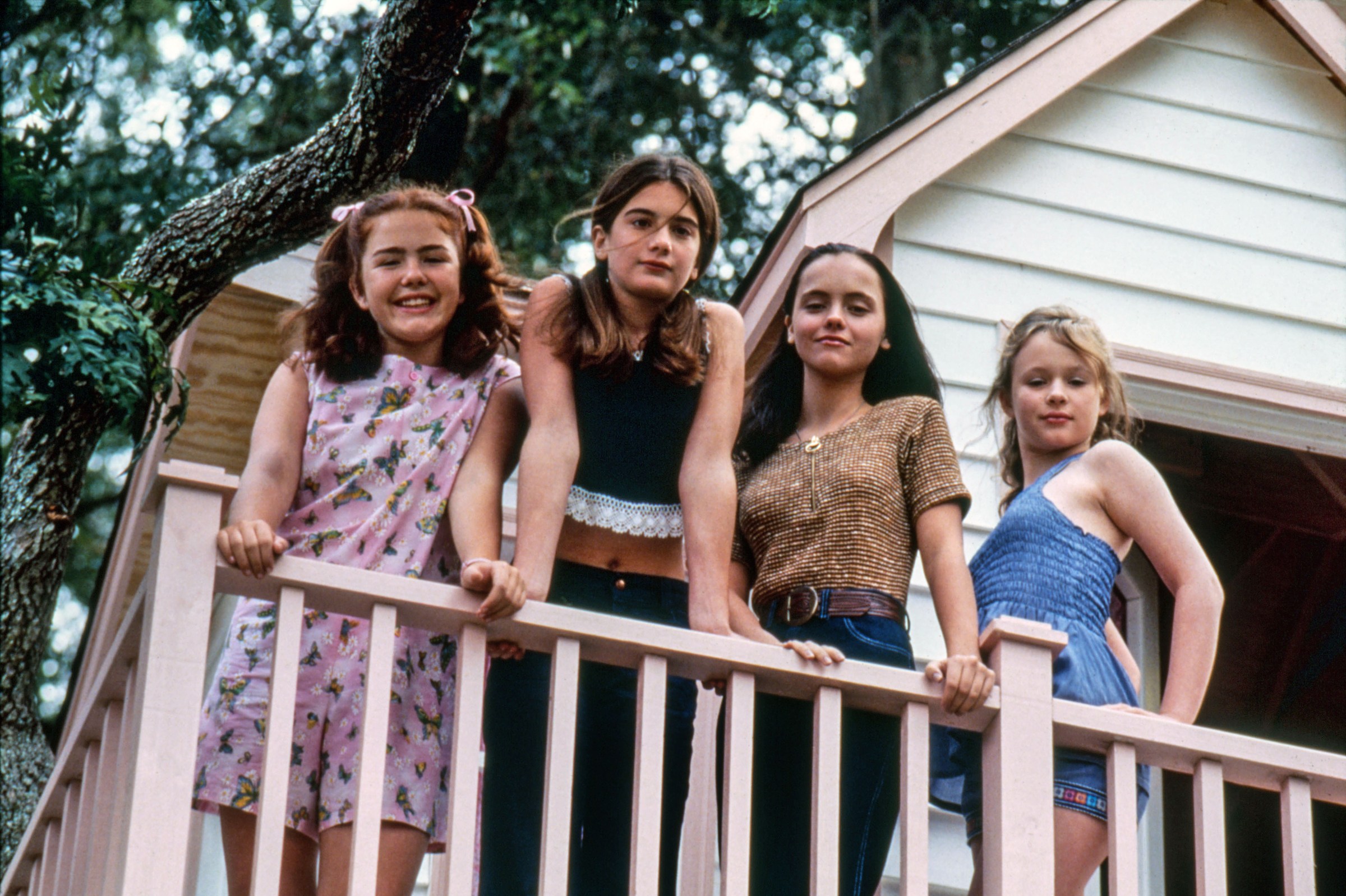 In Now and Then four girls lean on the railing of a tree house