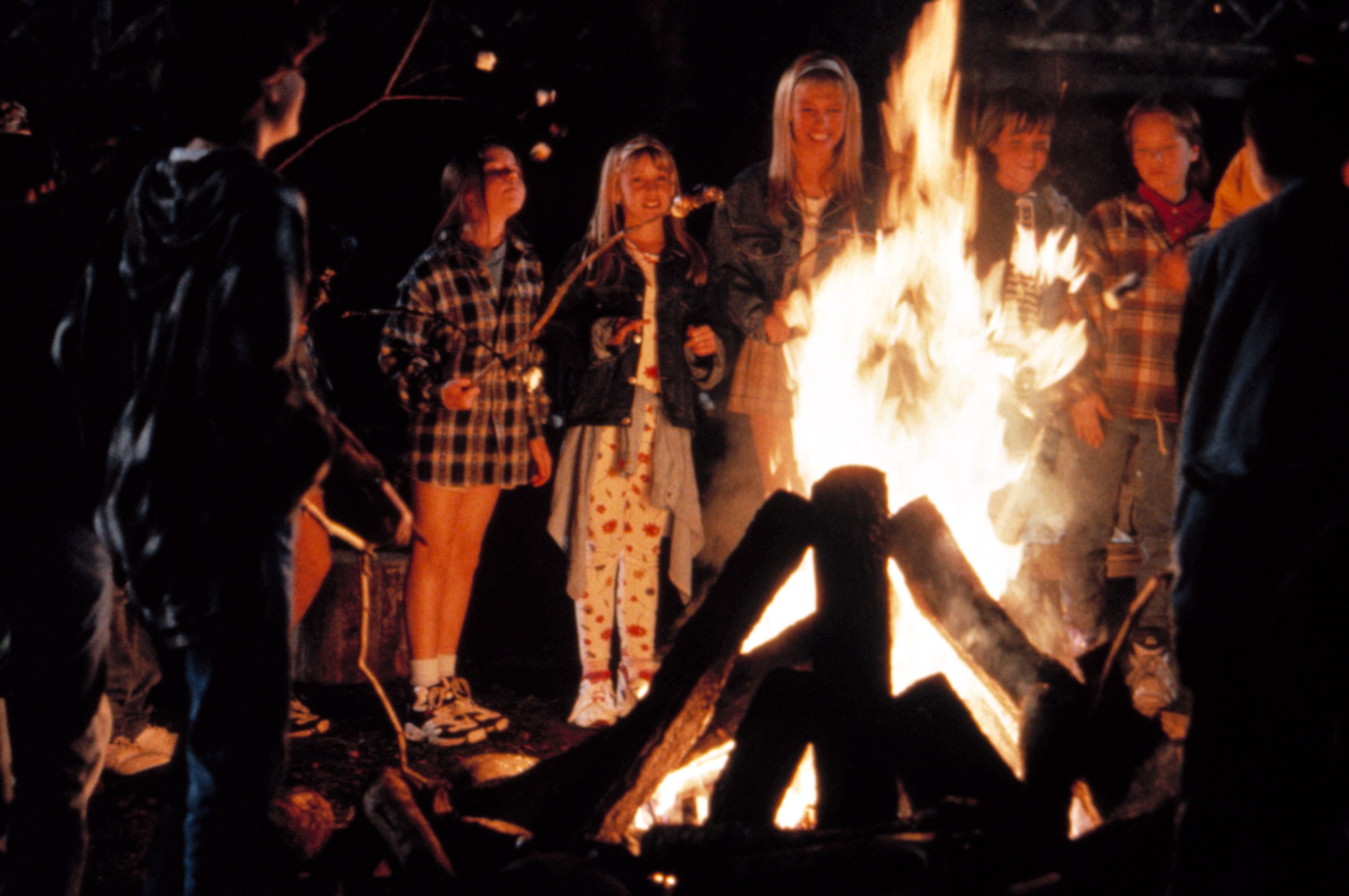 A group of teenagers and children gather around a campfire at Camp Nowhere