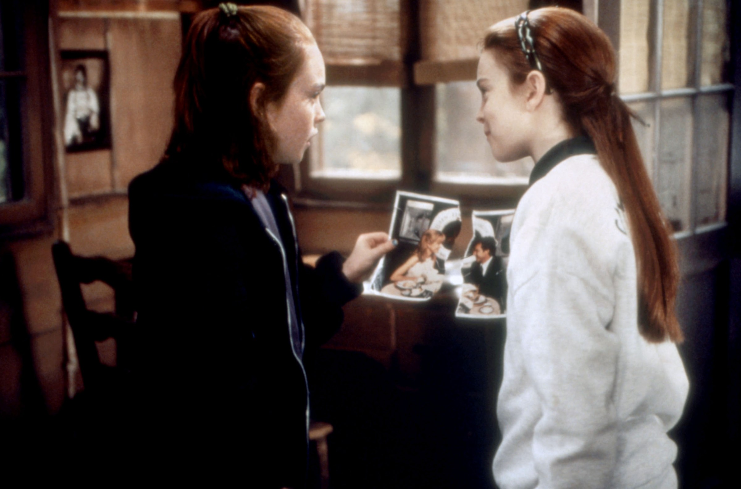 Two young Lindsay Lohans hold up the torn halves of a photo together in The Parent Trap