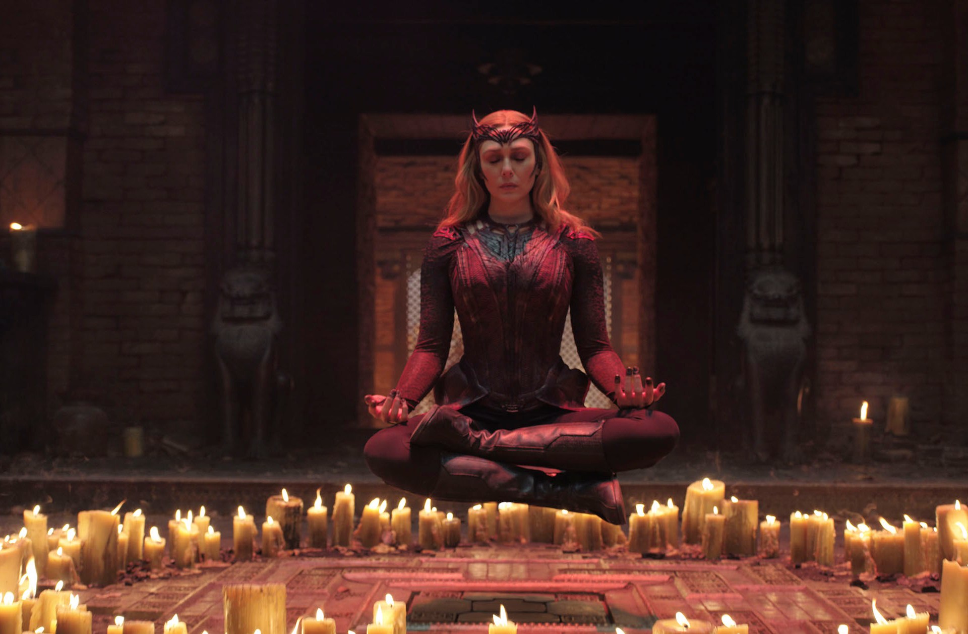 Elizabeth Olsen as Wanda Maximoff floats through the air in the lotus position, eyes closed, above a circle of candles in Doctor Strange in the Multiverse of Madness.