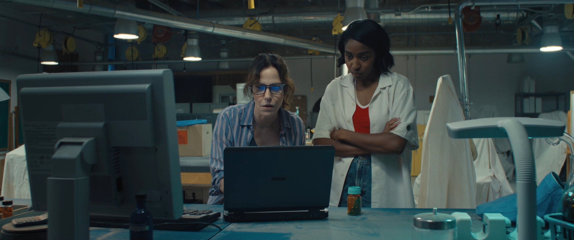 Two women stare intently at a computer screen in a cluttered lab in Omni Loop.