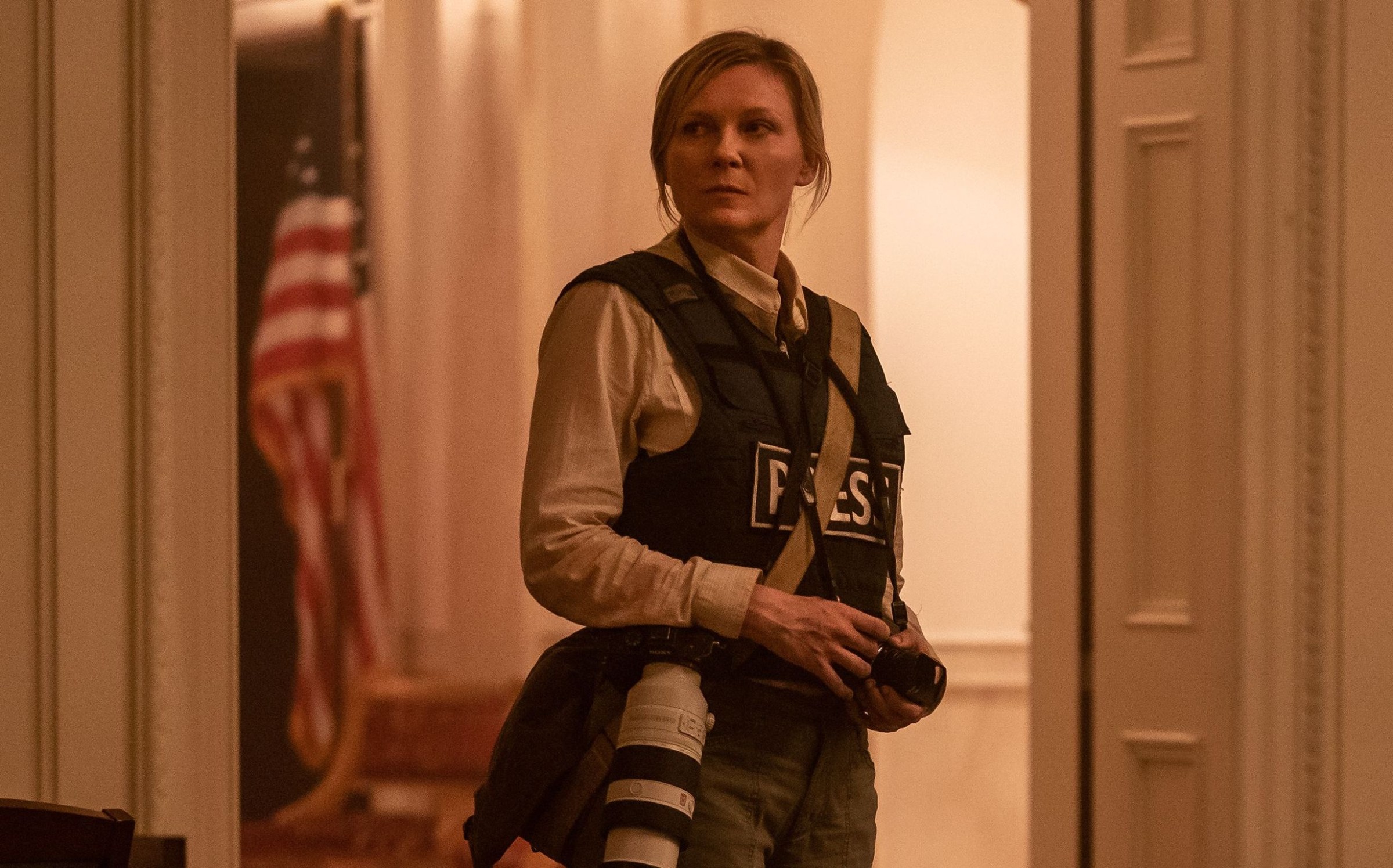 Kirsten Dunst in a “Press” bulletproof vest stands in the White House during the Civil War