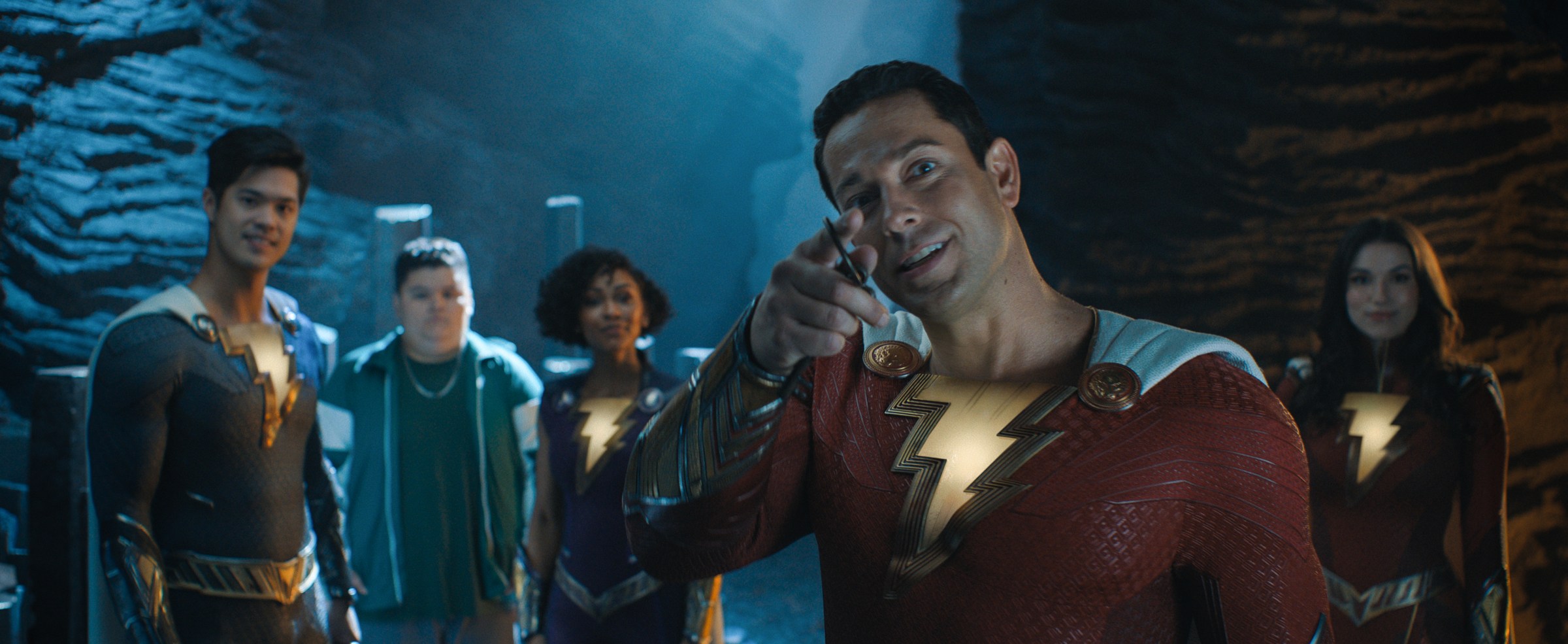 Zachary Levi as Shazam points into the camera and smiles, with members of his hero family behind him, in Shazam! Fury of the Gods