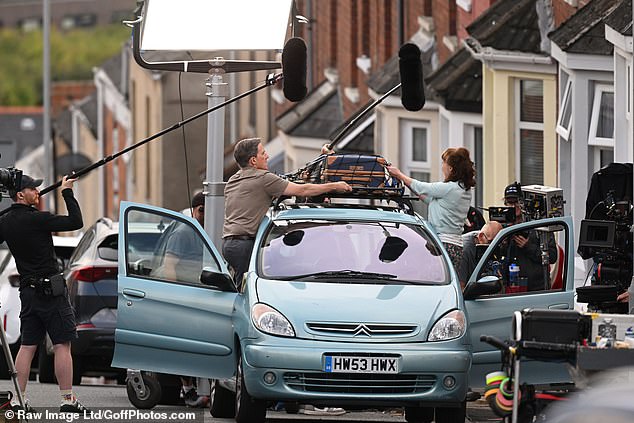 In one scene, Rob and his co-star Melanie Walters are seen strapping a suitcase to the roof of their blue Volvo