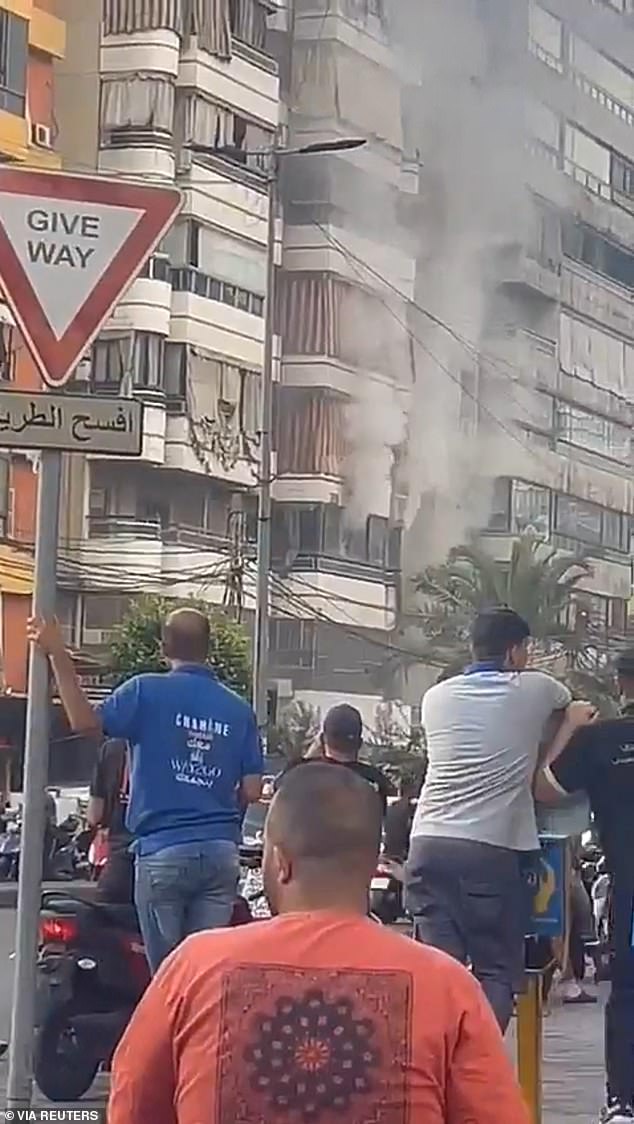 Crowds watch as smoke rises from a building after an explosion, while portable radios used by Hezbollah explode in southern Lebanon and Beirut