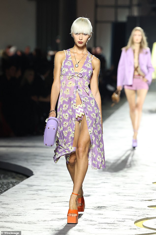 Iris Law struts down the runway in a revealing light purple dress with a yellow floral pattern over purple and yellow bikini bottoms at the Versace show during Milan Fashion Week on Friday night