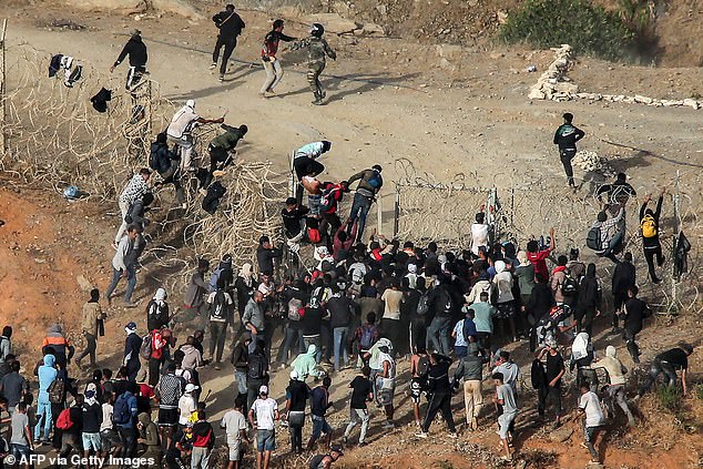 Migrants storm a barbed wire fence as they attempt to cross the land border into the Spanish enclave of Ceuta in Africa, near Fnideq in northern Morocco on September 15