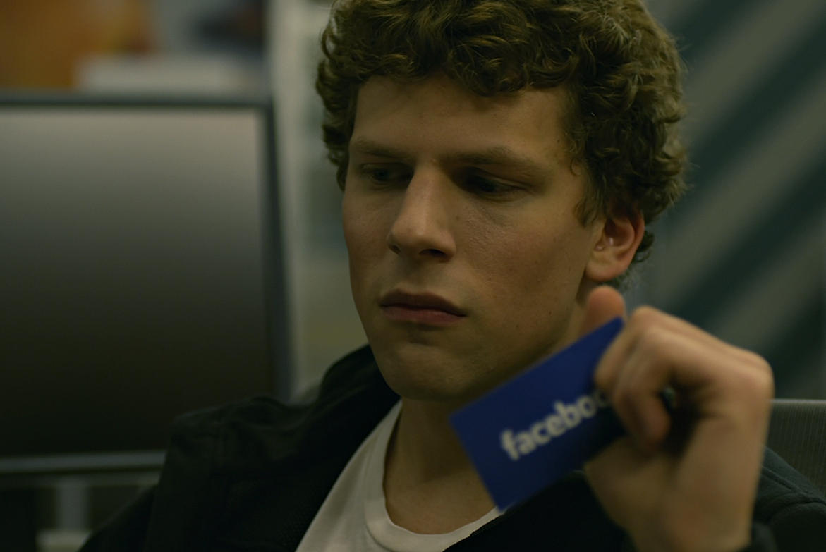 Jesse Eisenberg's Mark Zuckerberg ponders his company in a swivel chair while holding a Facebook business card in The Social Network