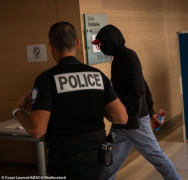 A suspect arrives in the courtroom with a police officer on September 20