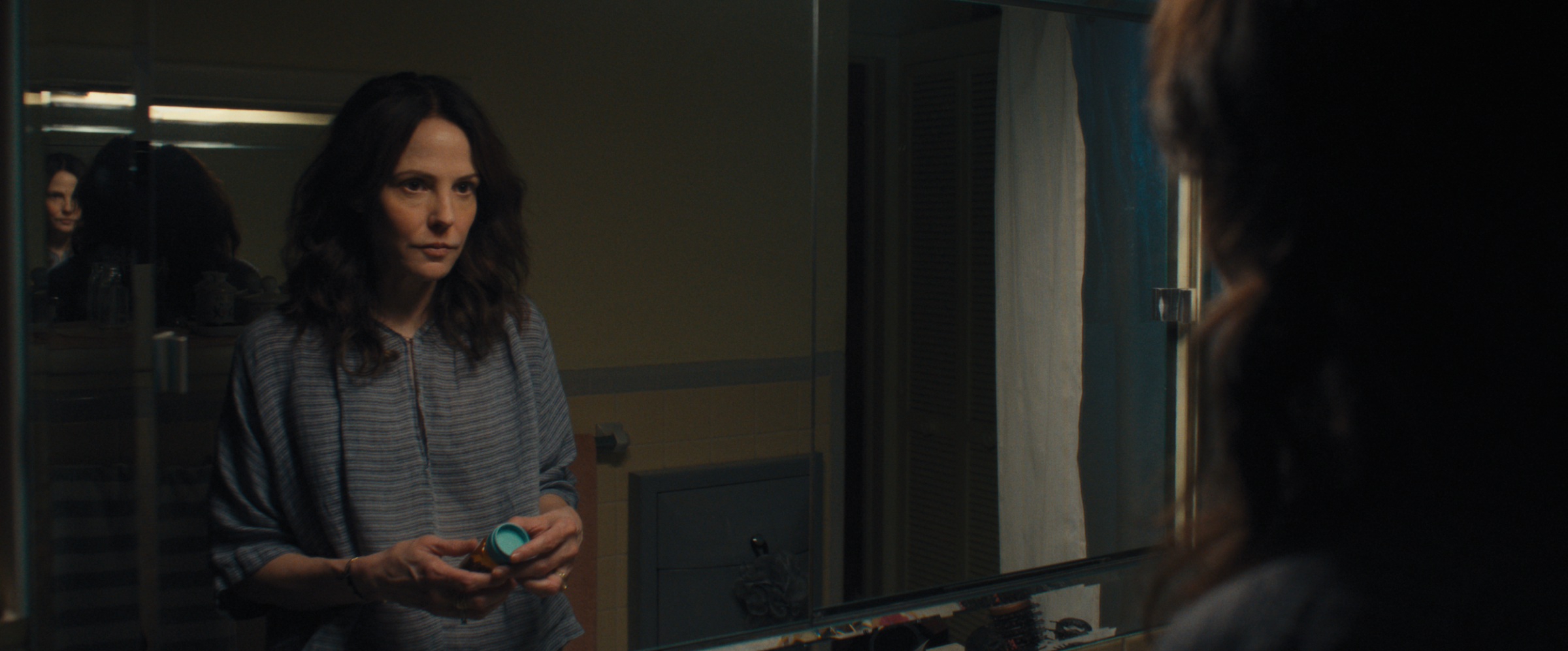 Mary-Louise Parker holds a bottle of pills and looks into a mirror in Omni Loop.