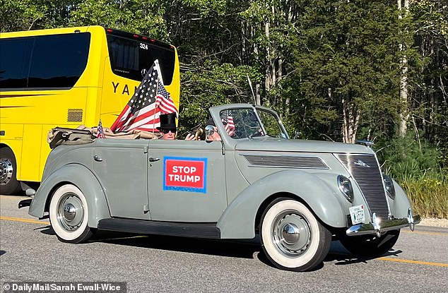 A man in a top hat drives a car with a 'Stop Trump' sign in New Hampshire