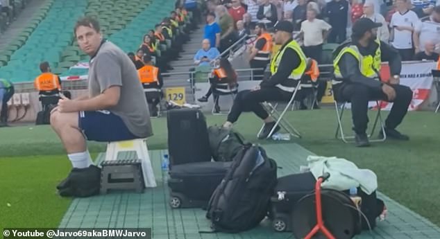 The YouTuber shows himself sitting next to security guards on the side of the field