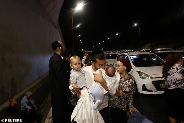 A man holds children as people take cover during an air raid, amid cross-border hostilities between Hezbollah and Israel, in central Israel on October 1