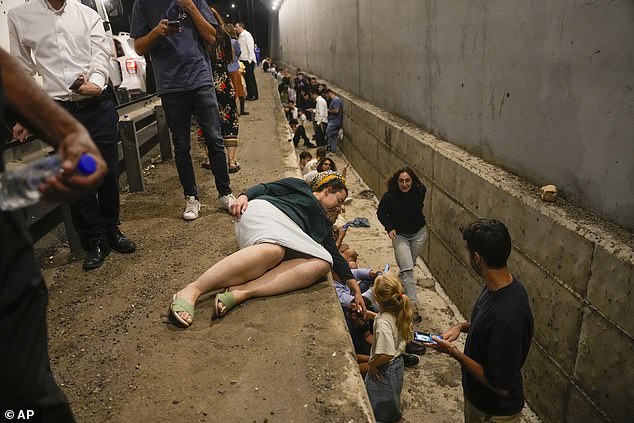 People take cover on the side of a road as a siren sounds to warn of incoming missiles fired from Iran on a highway in Shoresh, between Jerusalem and Tel Aviv in Israel, Tuesday, October 1, 2024