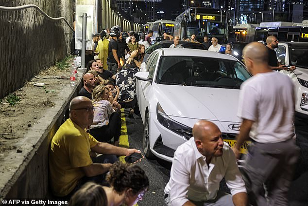 People take cover behind vehicles under a bridge on the side of a highway in Tel Aviv on October 1