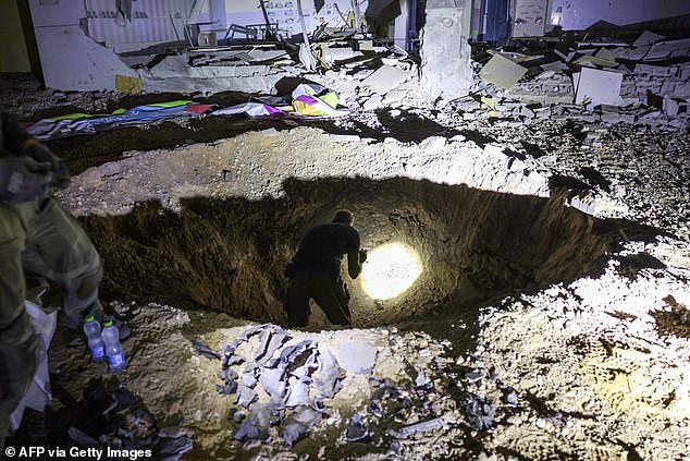 Members of the Israeli Home Front Command and police inspect a crater left by an exploded projectile in a badly damaged school building in the southern city of Gedera in Israel on October 1, 2024