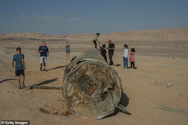 People take photos of and stand on the remains of a rocket in Arad, Israel.