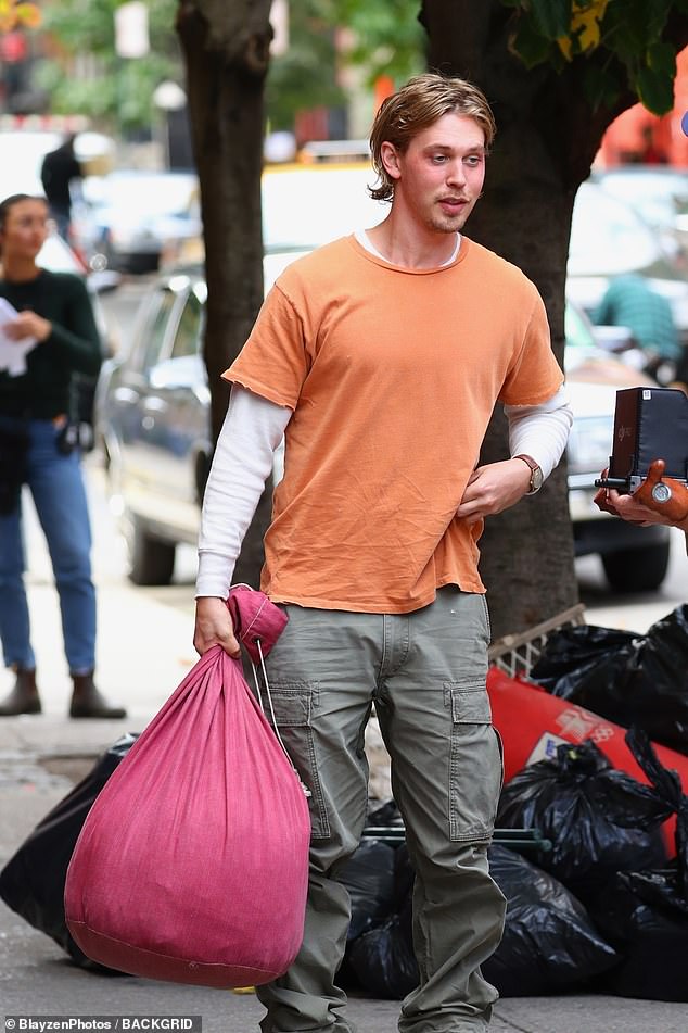 The handsome star walked down the dirty sidewalk in a worn orange T-shirt, a white thermal shirt and green cargo pants