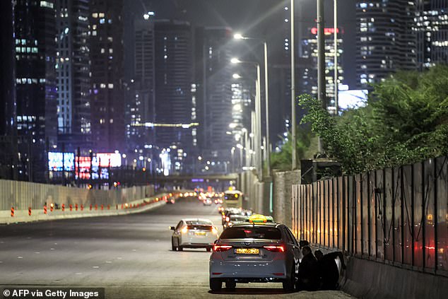 People take cover behind a vehicle parked along the highway in Tel Aviv