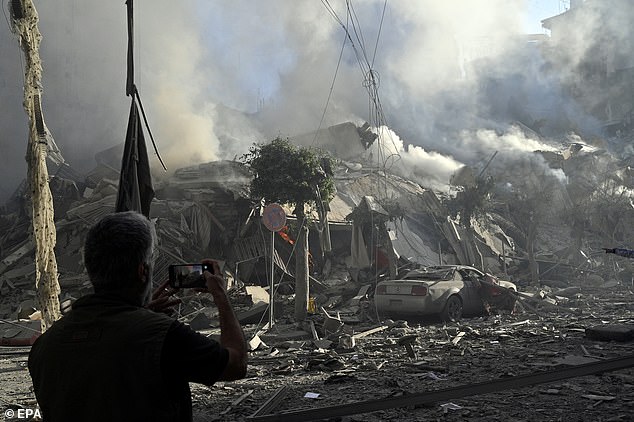 A man takes a photo as smoke rises from a damaged building after Israeli airstrikes in Dahieh, a southern suburb controlled by Hezbollah in Beirut, Lebanon