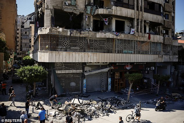 People and members of the press look at a damaged building at the site of an Israeli attack on the Bachoura neighborhood of central Beirut