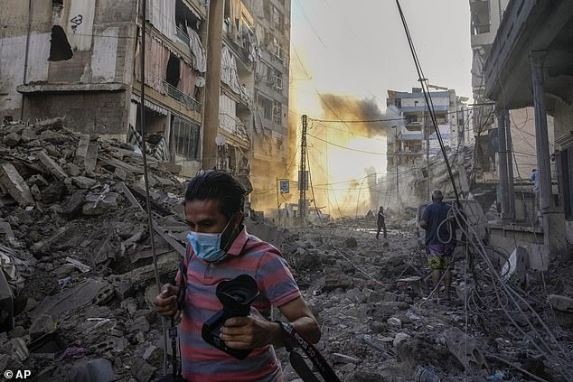 A photographer takes cover as smoke rises in the background after an Israeli airstrike in Dahiyeh, Beirut, Lebanon, Friday, October 4, 2024