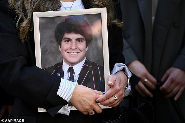 A portrait of James Tsindos is held aloft as Shari Liby, Slater and Gordon Medical Law Legal Counsel speak to the media during the inquest into the death