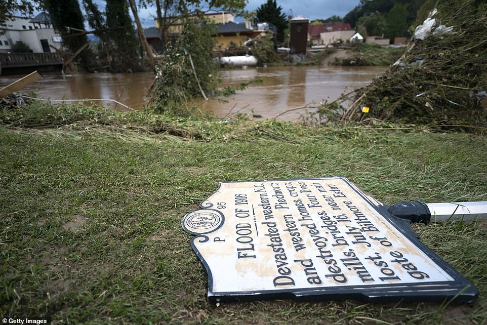 A sign commenting on the 1916 flood lies on the ground next to a flooded waterway near Biltmore Village in the aftermath of Hurricane Helene on September 28, 2024 in Asheville