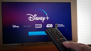 A man holding a remote control towards a screen with the Disney Plus logo