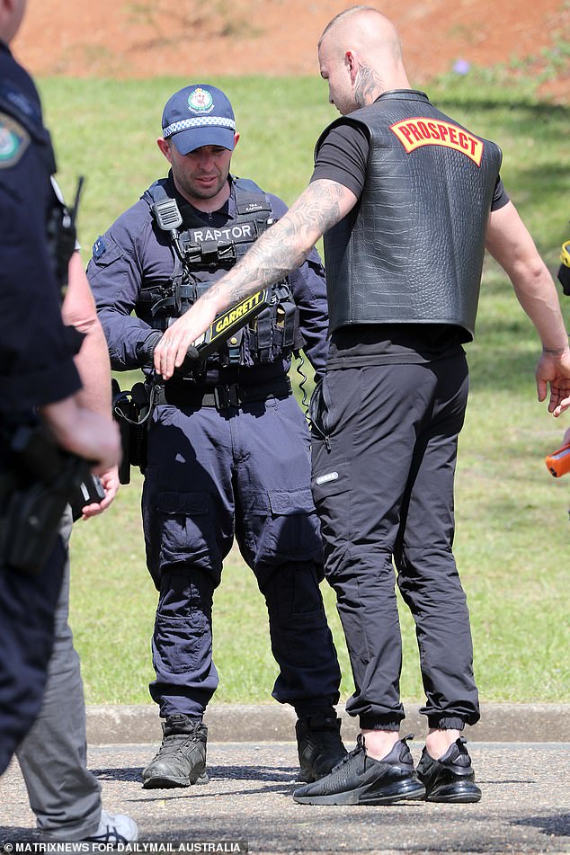 Outside the funeral, a man is scanned by a metal detector